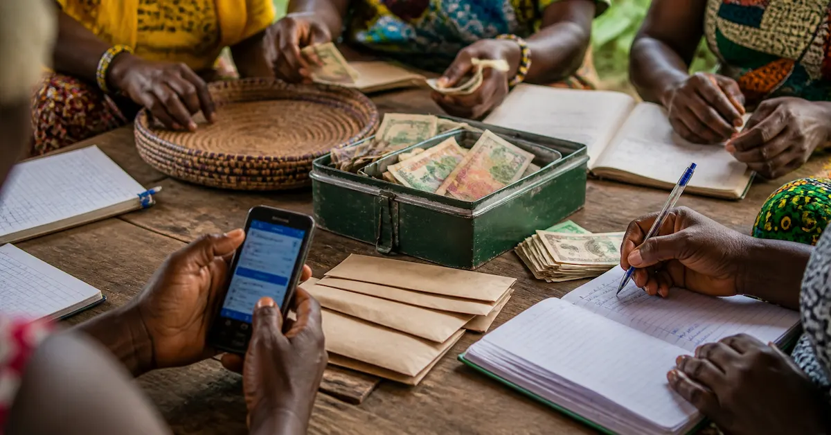 A savings group recording contributions beside a cash box